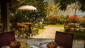 Un comedor con mesas y sillas, rodeado de exuberante vegetación y vista al mar.