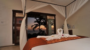 Un dormitorio con cama, dosel y vista al océano al atardecer.