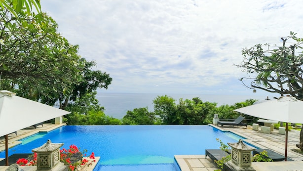 Una piscina con vistas al mar, rodeada de vegetación y estructuras de piedra.
