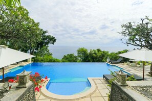 A swimming pool with a view of the sea, surrounded by greenery and stone structures.