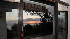 Una habitación con vista al atardecer sobre el océano, una puerta de madera y una puerta de cristal que da al exterior.