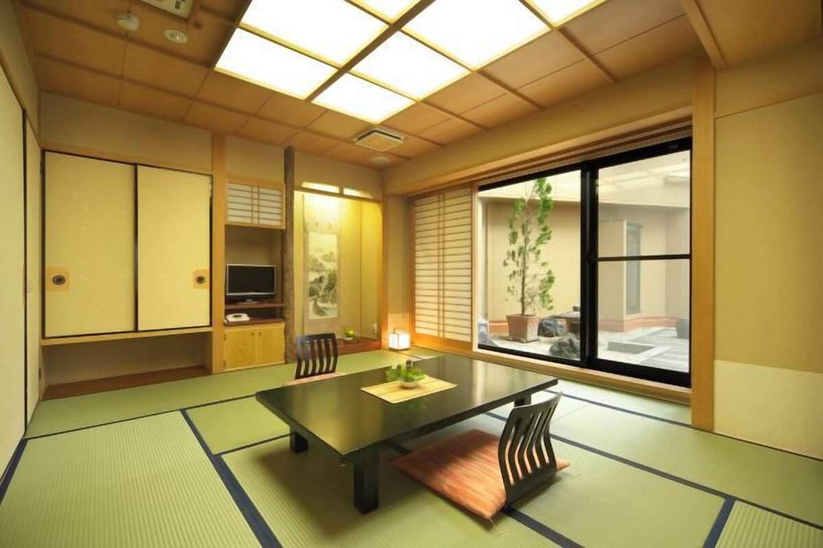 Una habitación japonesa tradicional con suelo de tatami, una mesa baja, puertas correderas y un ventanal con vistas.