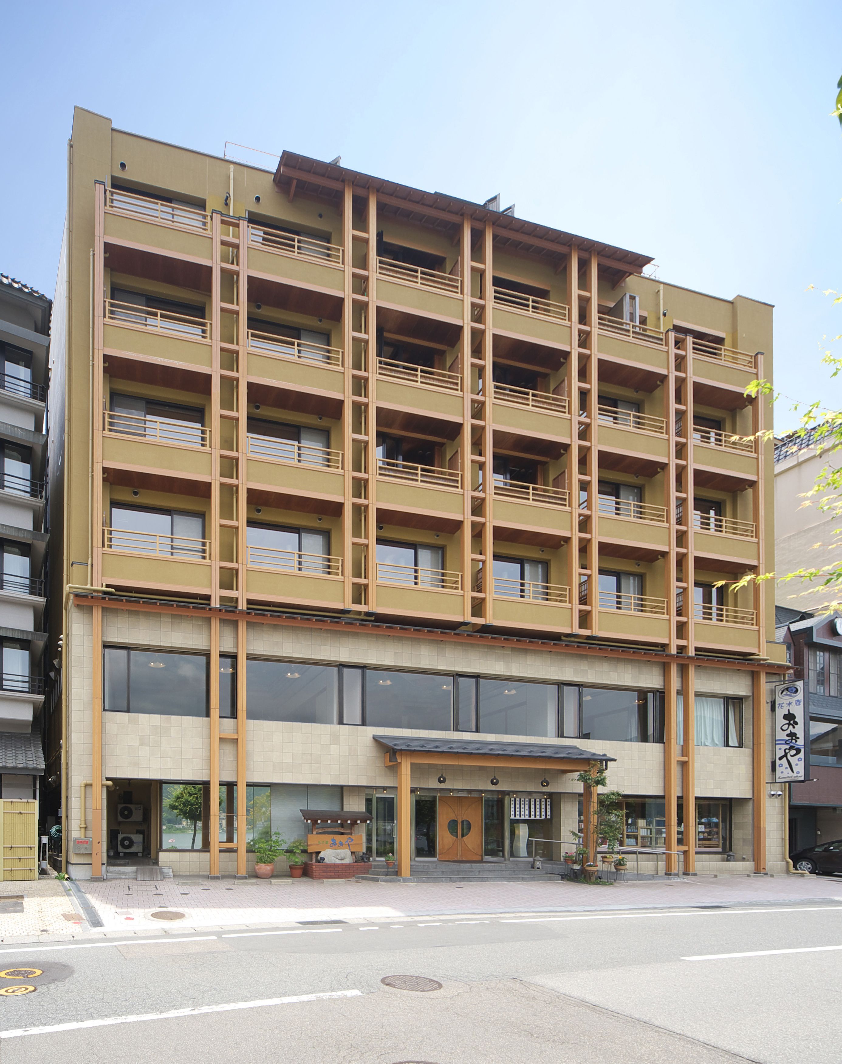 Un immeuble à plusieurs étages doté d’une architecture moderne, avec des balcons à chaque niveau et une entrée au rez-de-chaussée agrémentée d’une porte en bois.