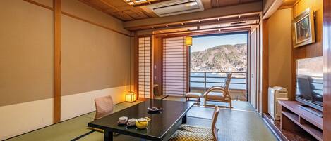 A traditional Japanese room with tatami flooring, a low table with tea sets, a television, and a view of a mountainous landscape.