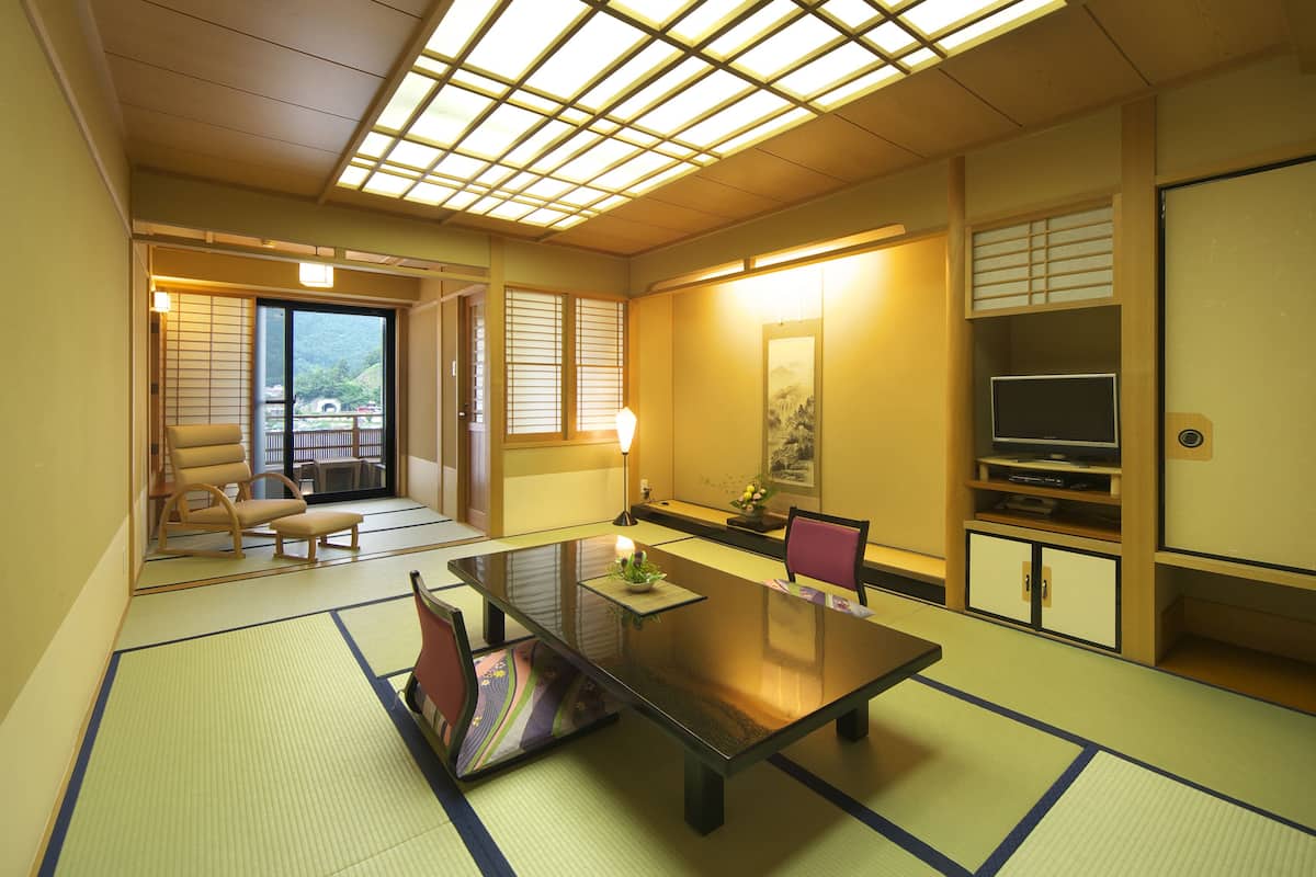 A traditional Japanese room with tatami flooring, a low table, chairs, a television, and sliding doors.