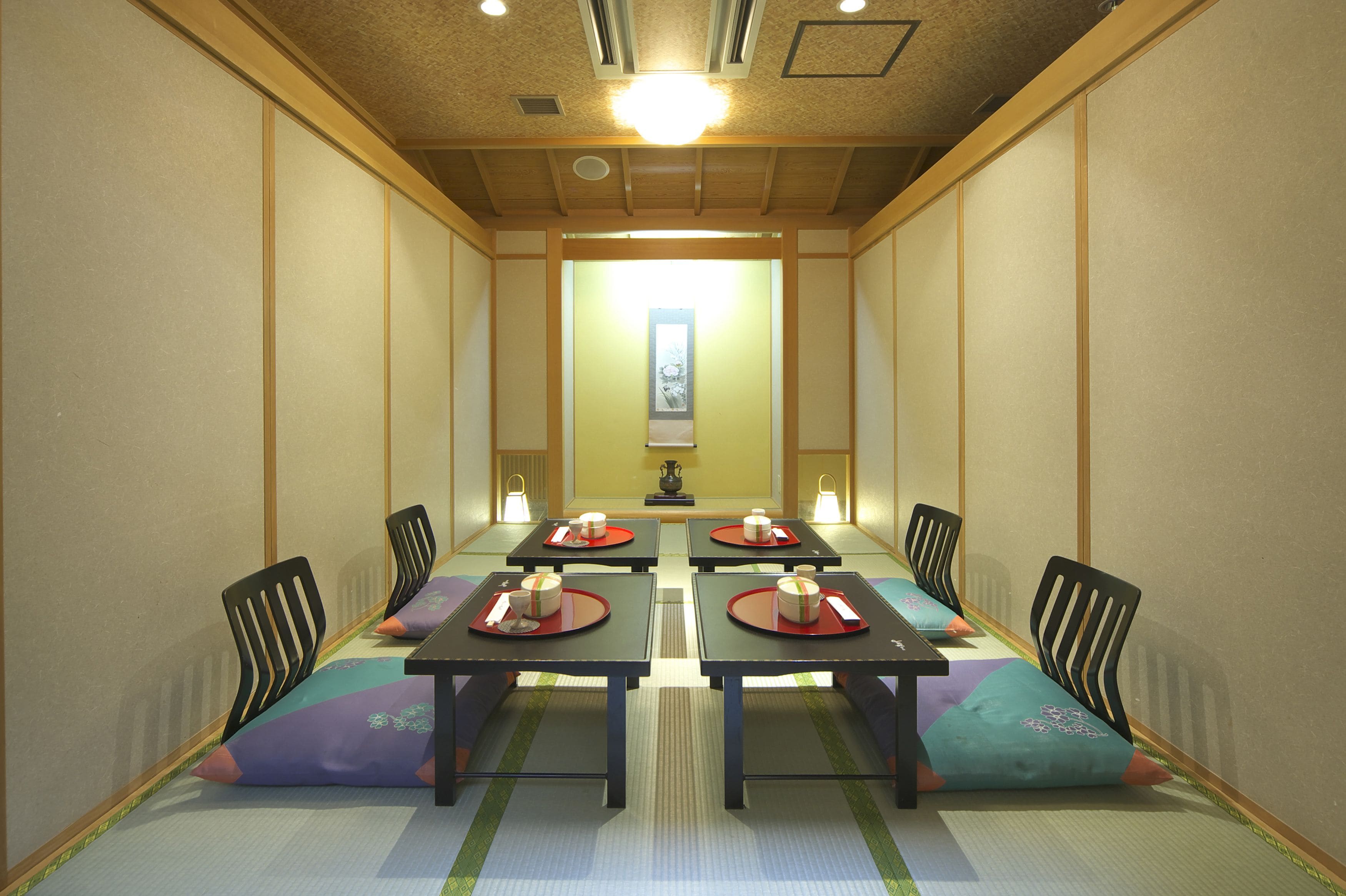 A traditional Japanese-style dining room with tatami mats, low tables, and black chairs.