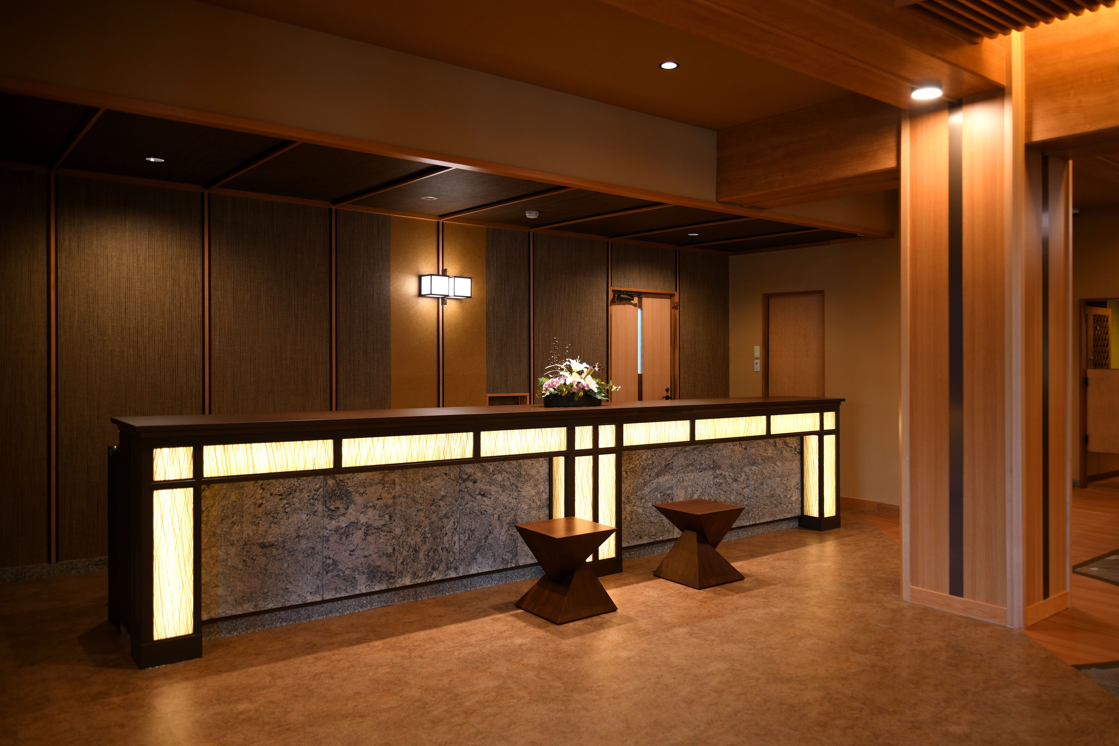 A reception area with a wooden reception desk, two small tables, and a wall-mounted light fixture.