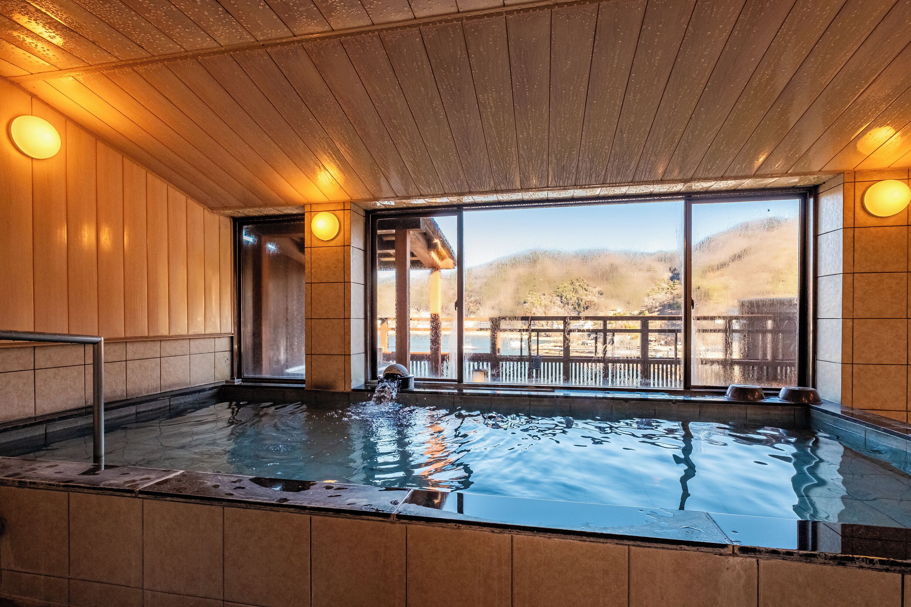 A hot tub with wooden walls and large windows overlooking a mountainous landscape.