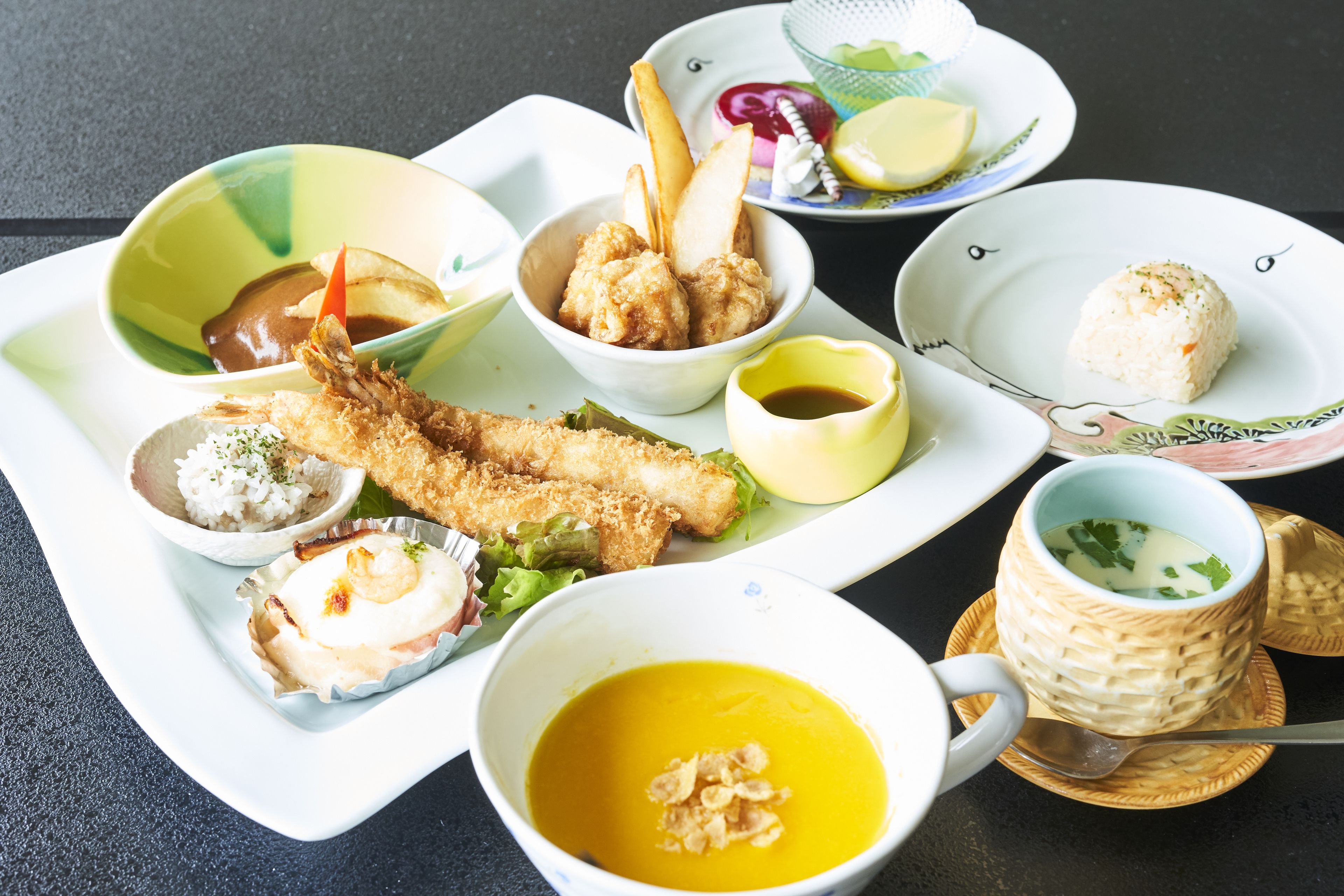 A variety of dishes including fried items, rice, and soup, served on multiple plates and bowls.