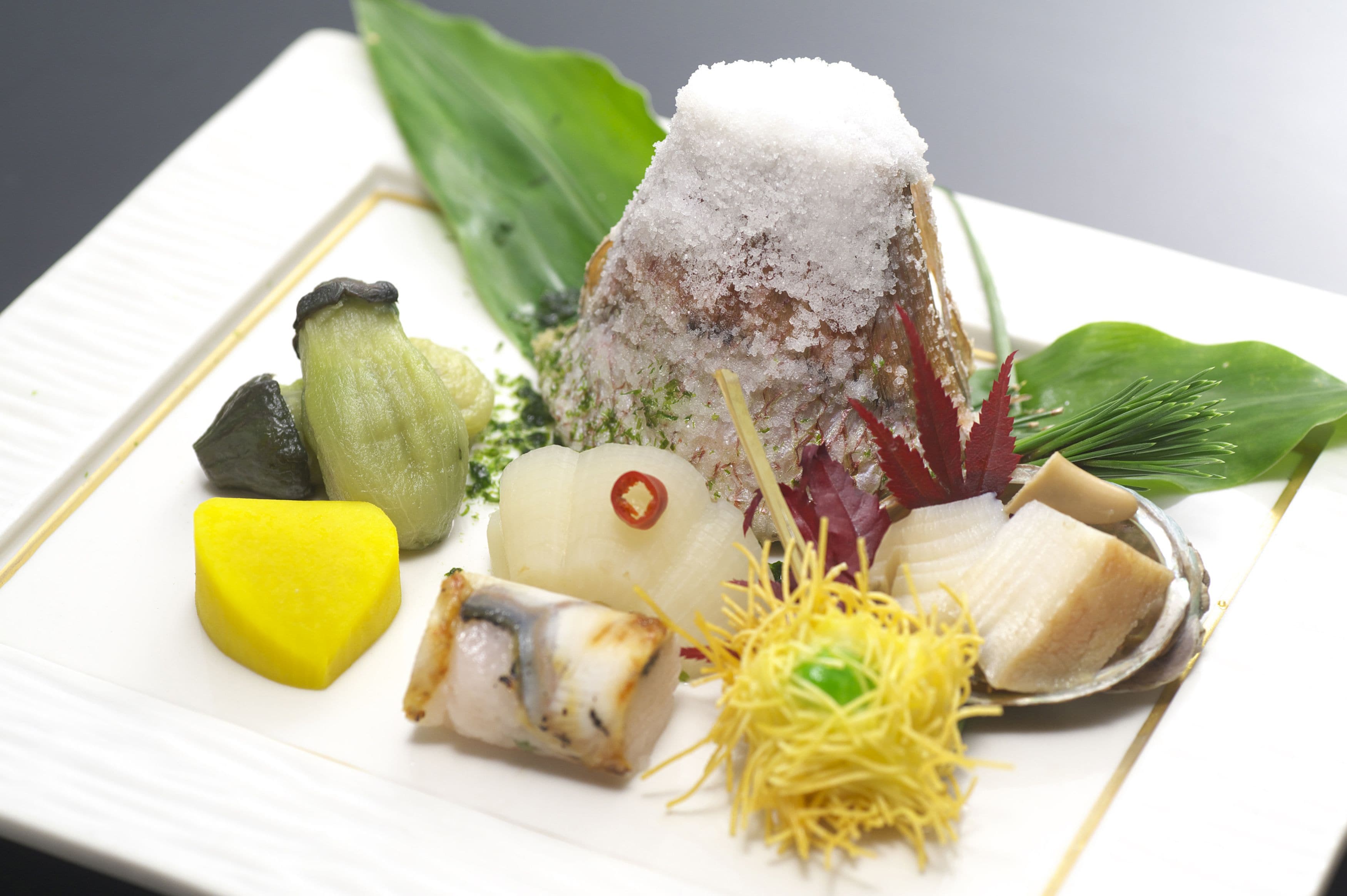 A plate of assorted food items including a mound of rice, a piece of fish, and various vegetables.