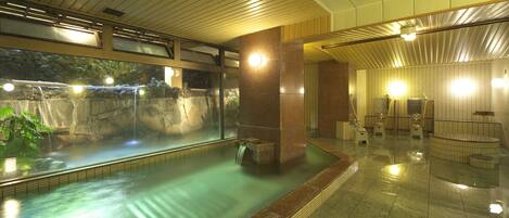 A spacious indoor swimming pool with a waterfall feature, surrounded by tiled walls and a wooden ceiling.