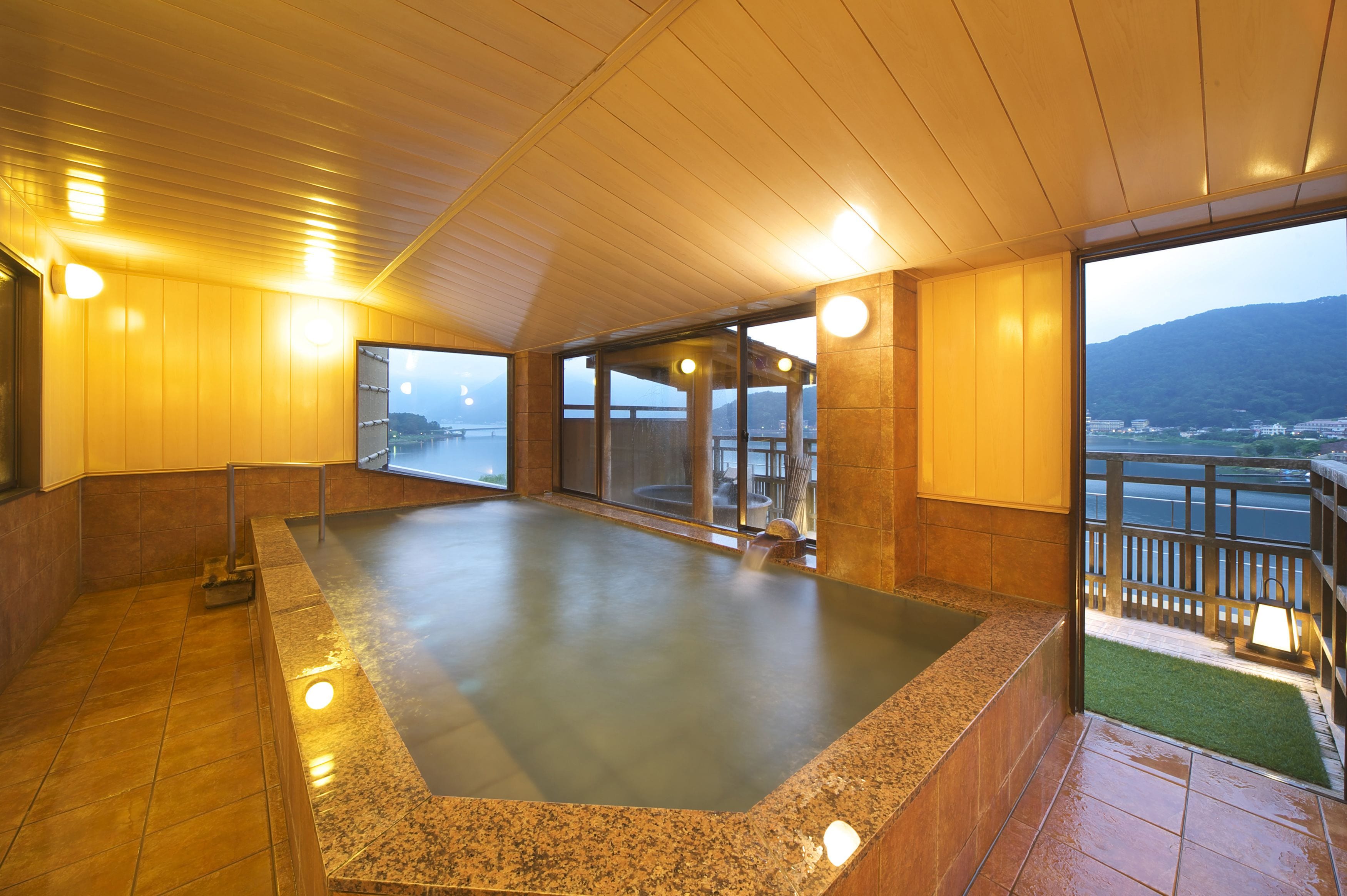Zona de spa con un jacuzzi, techo de madera y vistas a un puente y montañas.