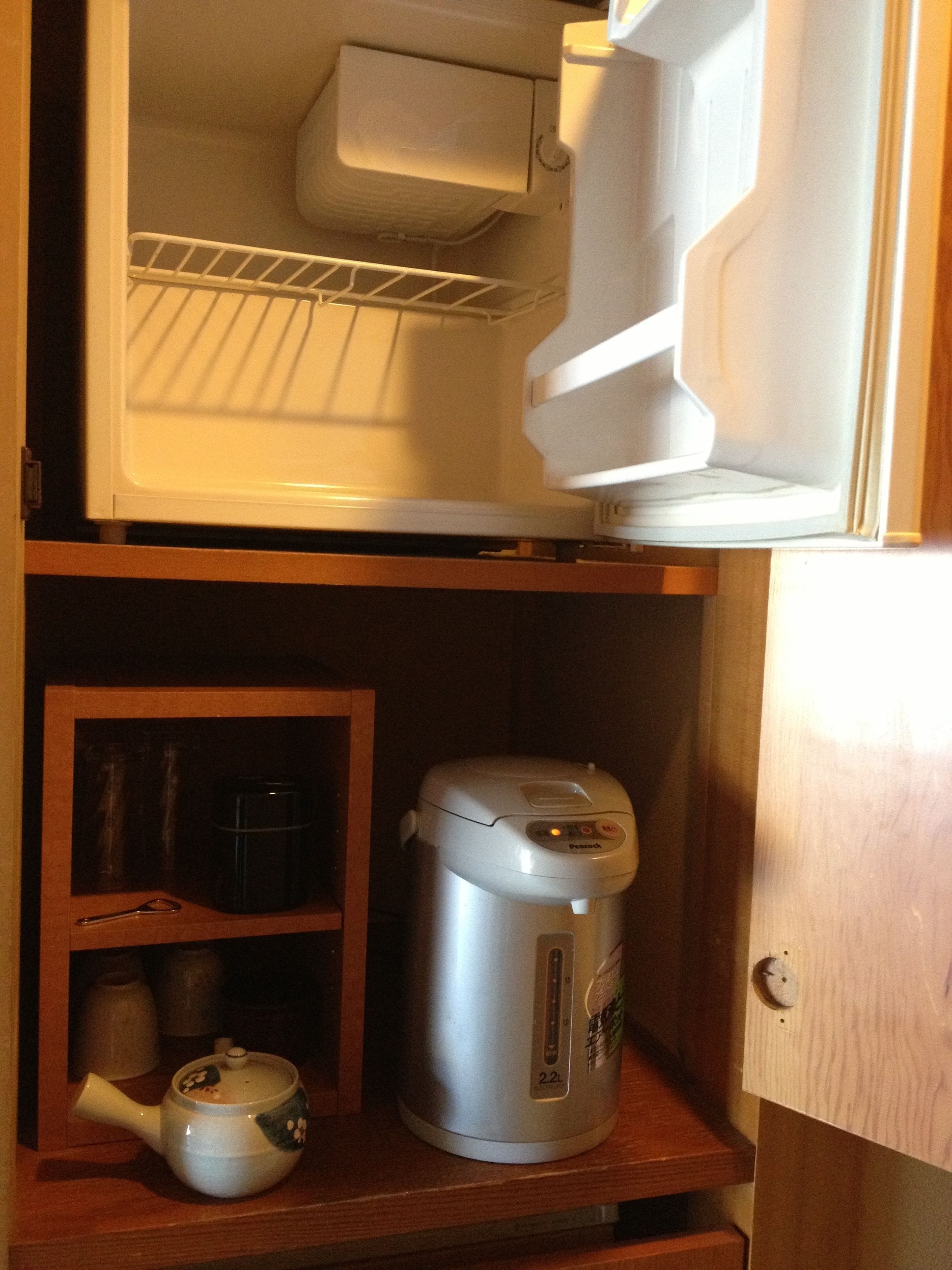 A kitchen with a microwave, a rice cooker, and a teapot on a wooden shelf.