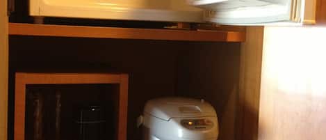 A kitchen with a microwave, a rice cooker, and a teapot on a wooden shelf.