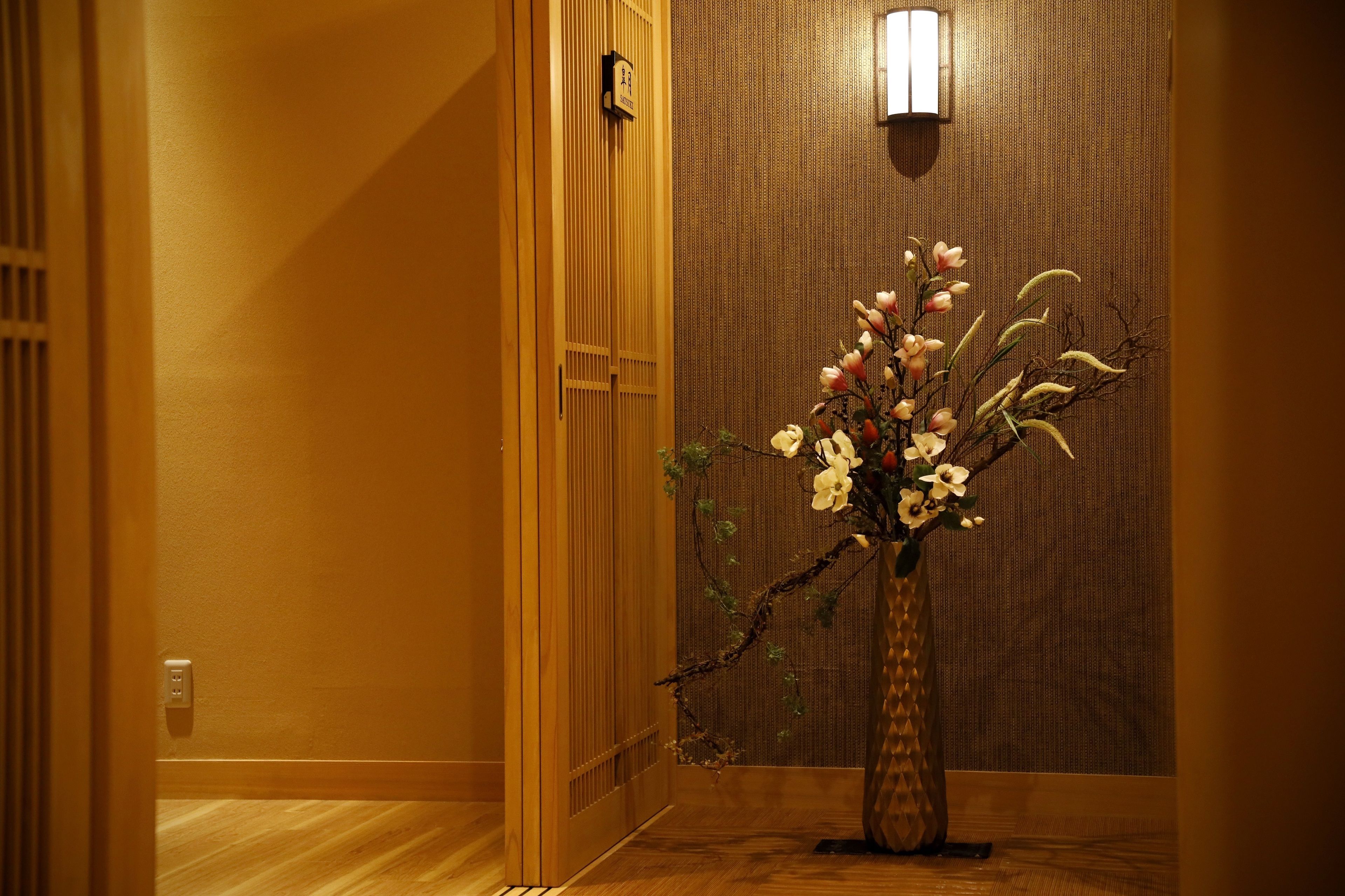 A hallway with a wooden floor, a wooden door, and a wall-mounted light fixture.