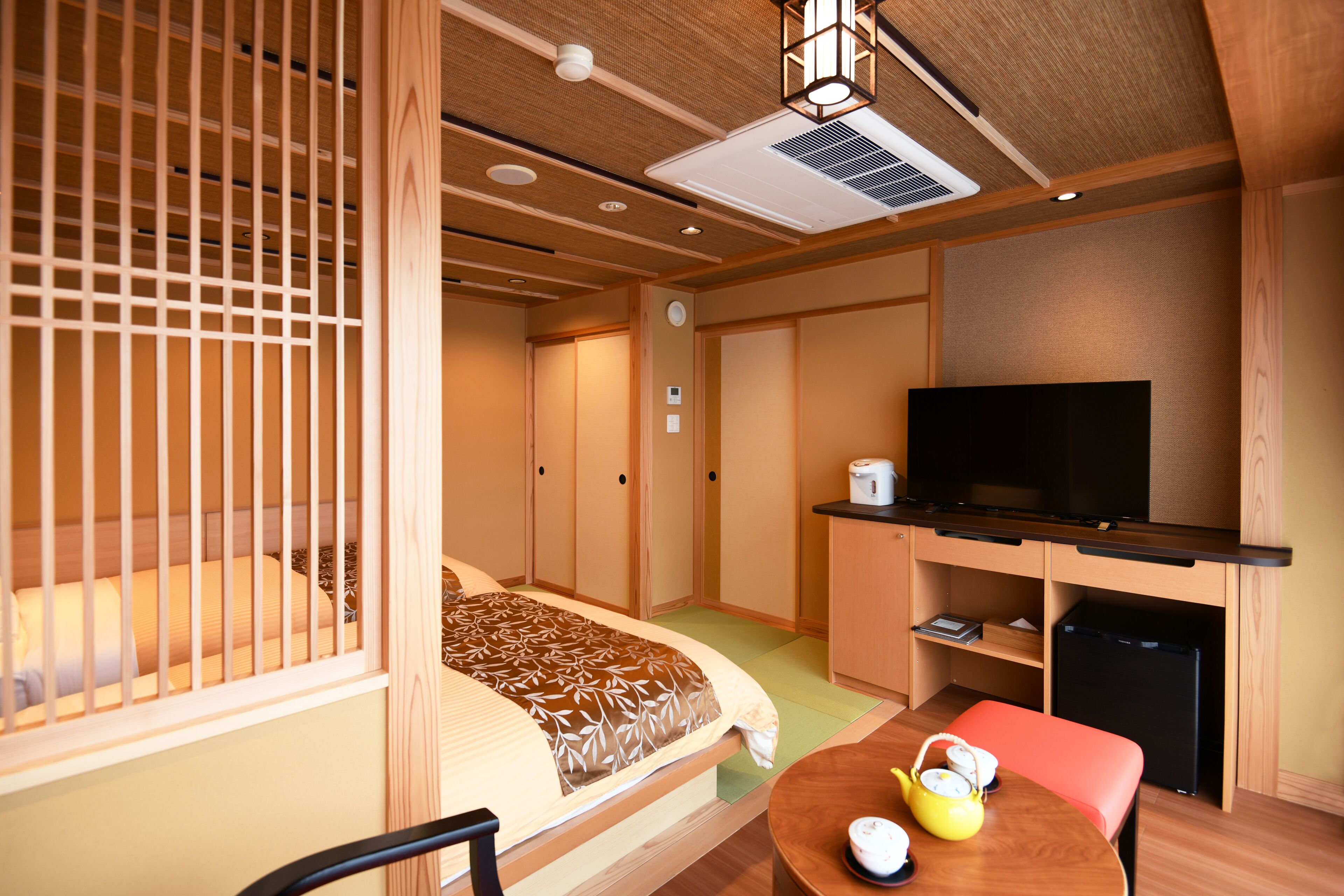 Habitación de hotel pequeña con cama, una mesita con tetera, televisor y zona de kitchenette.