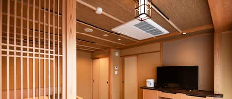 Habitación de hotel pequeña con cama, una mesita con tetera, televisor y zona de kitchenette.