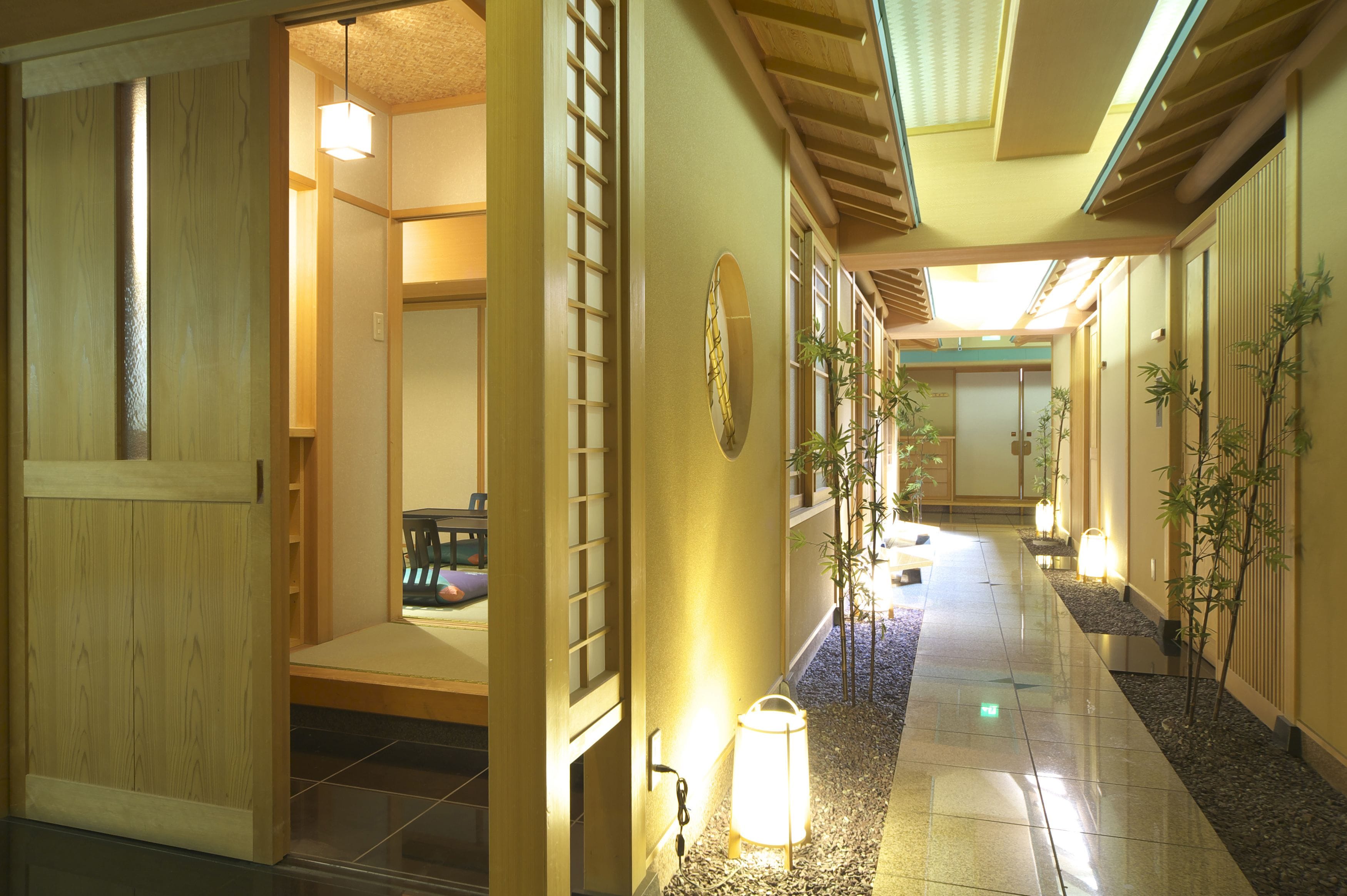 A traditional Japanese interior with sliding doors, tatami flooring, and a hallway with a tiled floor and potted plants.