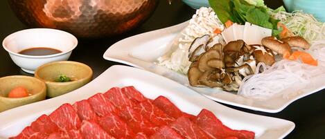 A table with various food items including sliced meat, mushrooms, and vegetables, accompanied by bowls of sauces.