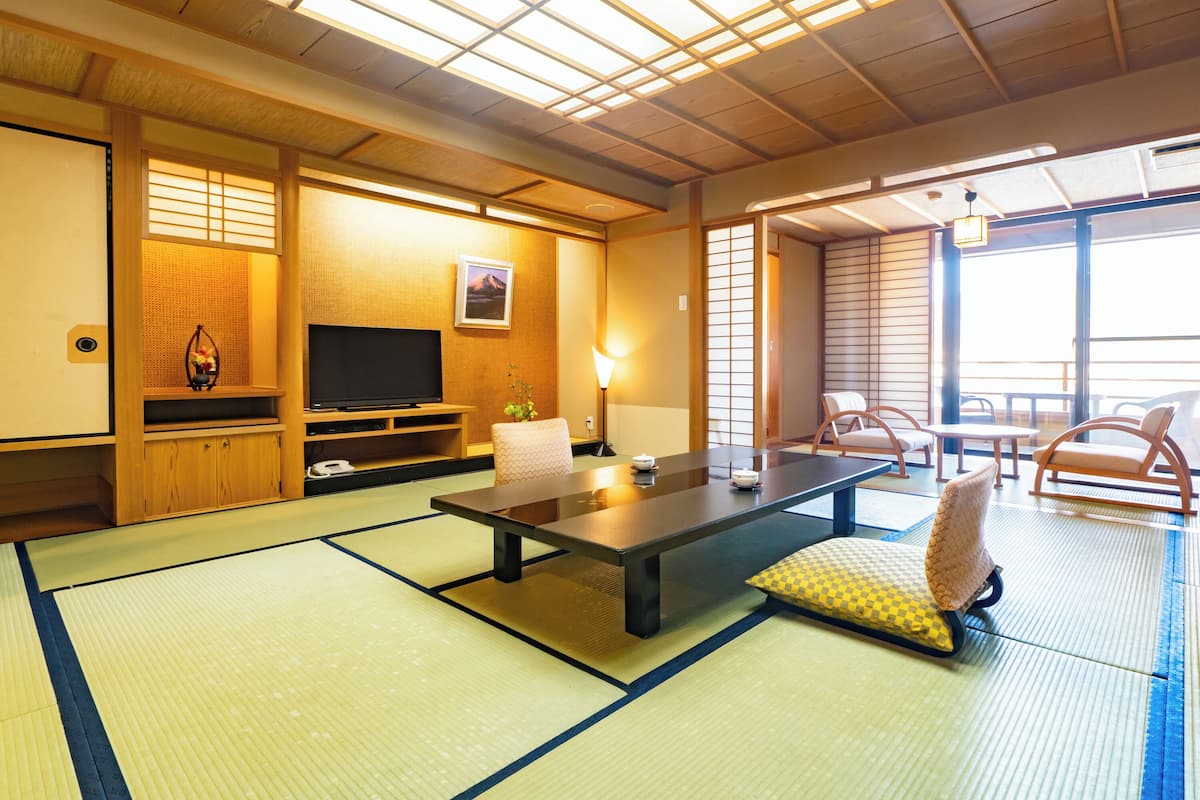 A traditional Japanese room with tatami flooring, a low table, cushions, a television, and sliding doors.