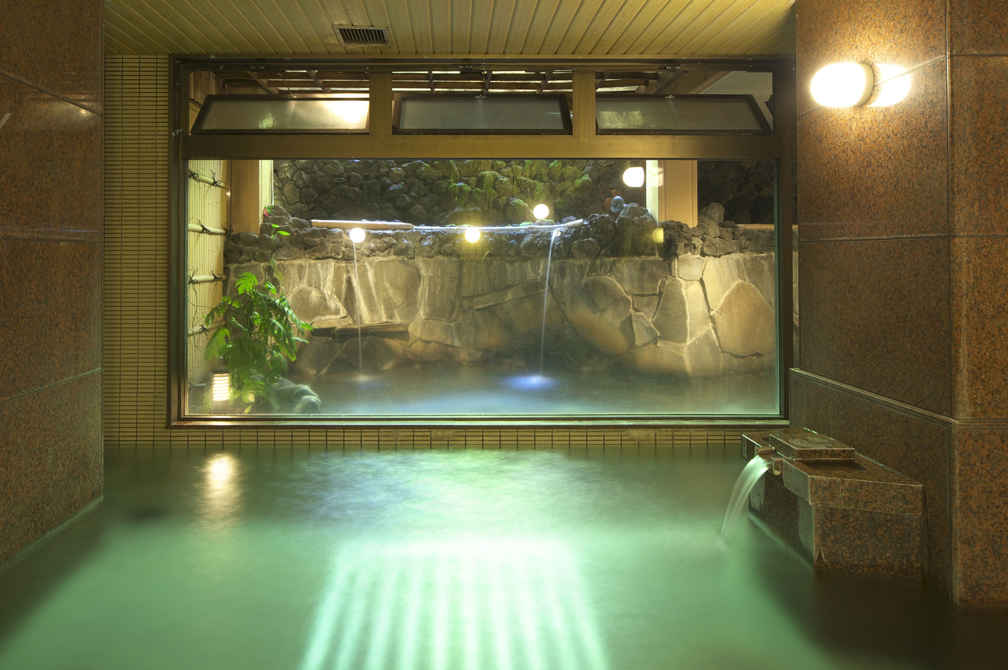 Een wellnessruimte met een ruime glazen overkapping, een waterval en een achtergrond van een stenen muur.