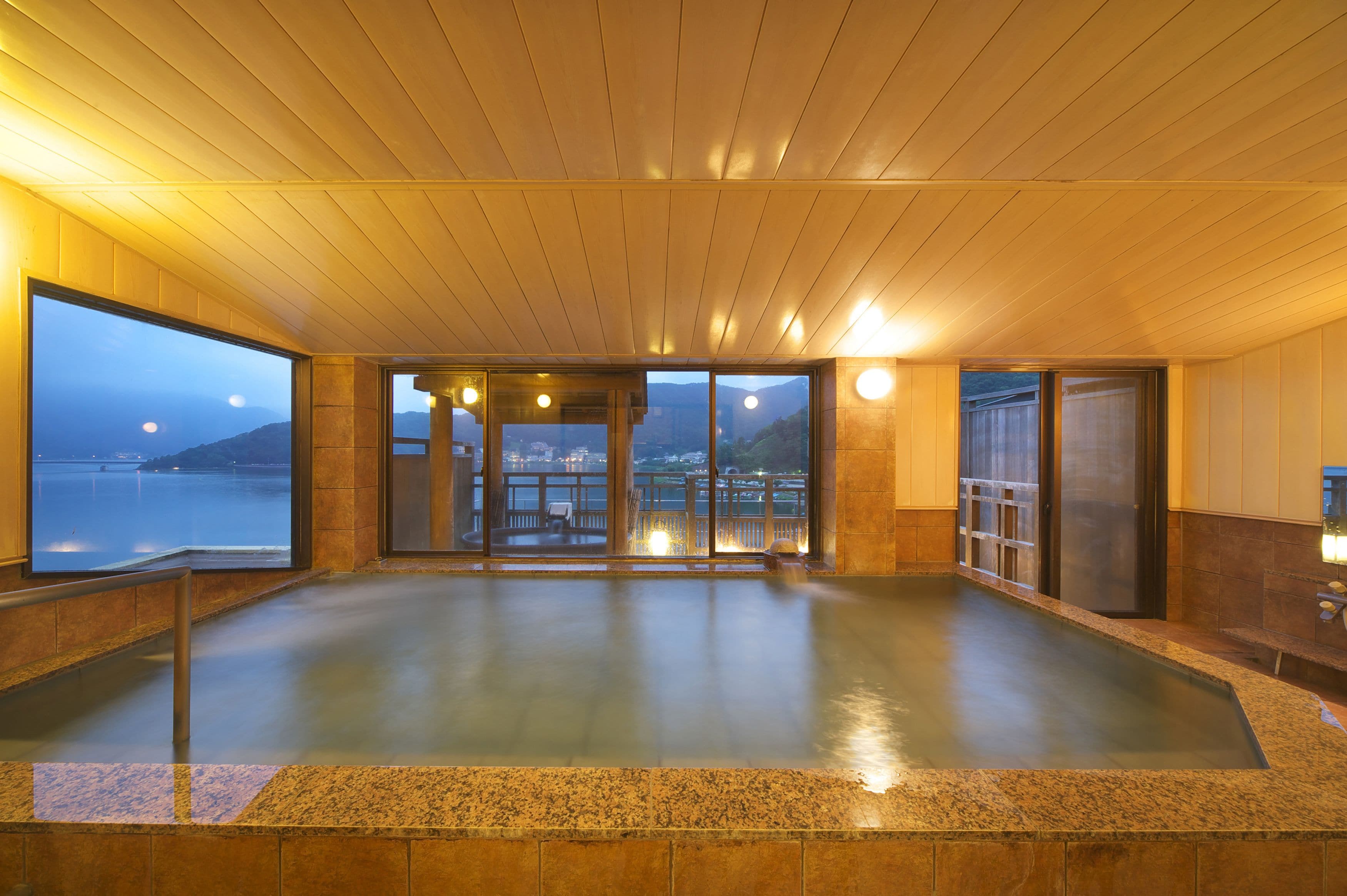 Un vaste espace intérieur abritant une piscine, avec vue sur la mer et les montagnes, un plafond en bois et des murs carrelés.
