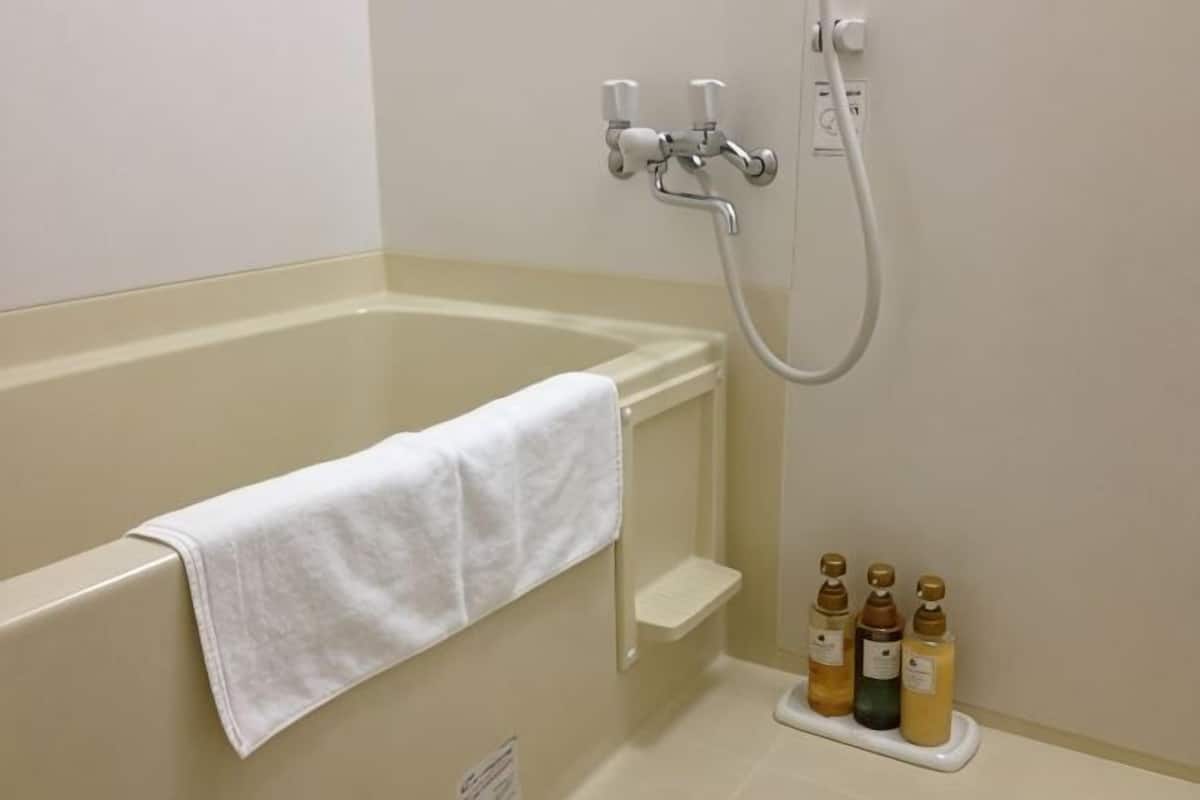 A bathroom with a bathtub, a towel rack, a showerhead, and a soap dispenser.