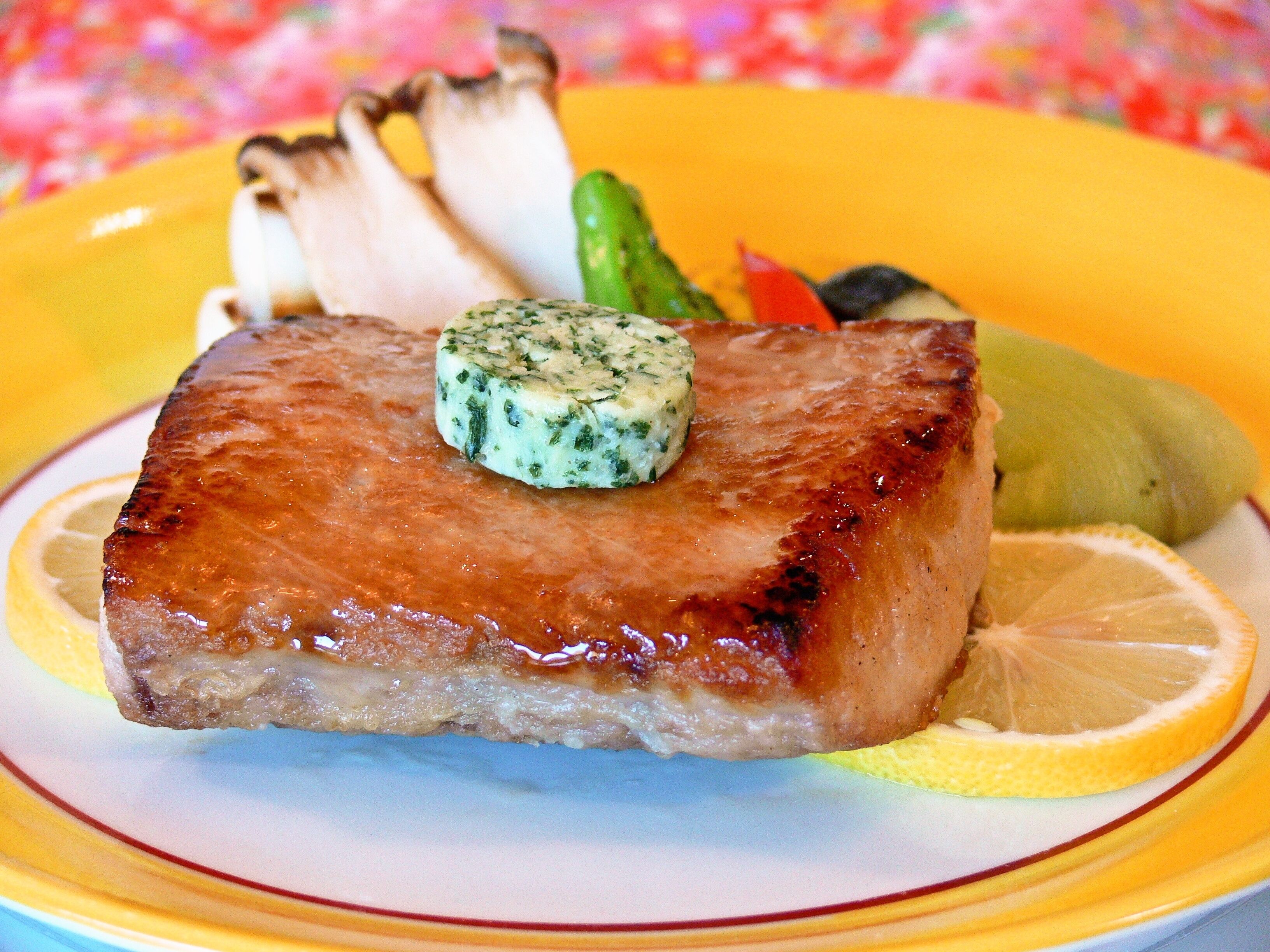 A plate with a grilled meat, a slice of lemon, and a dollop of herb butter.