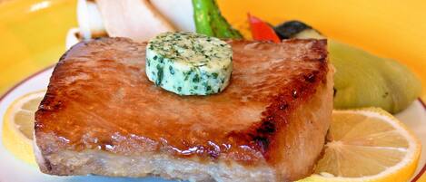 Ein Teller mit gegrilltem Fleisch, einer Zitronenscheibe und einem Klecks Kräuterbutter.