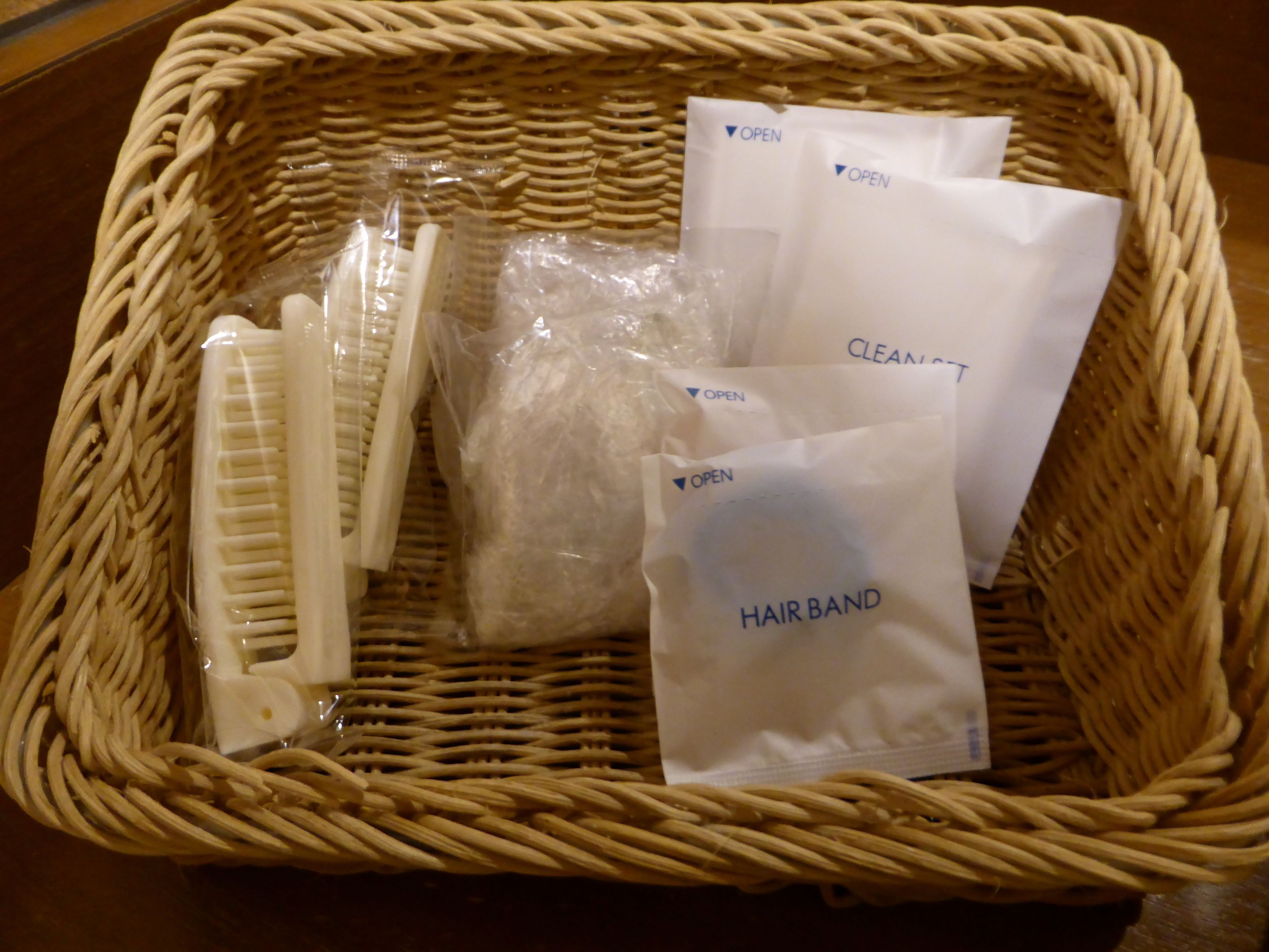 A wicker basket containing hairbrushes, a hairband, and a plastic bag with a label.