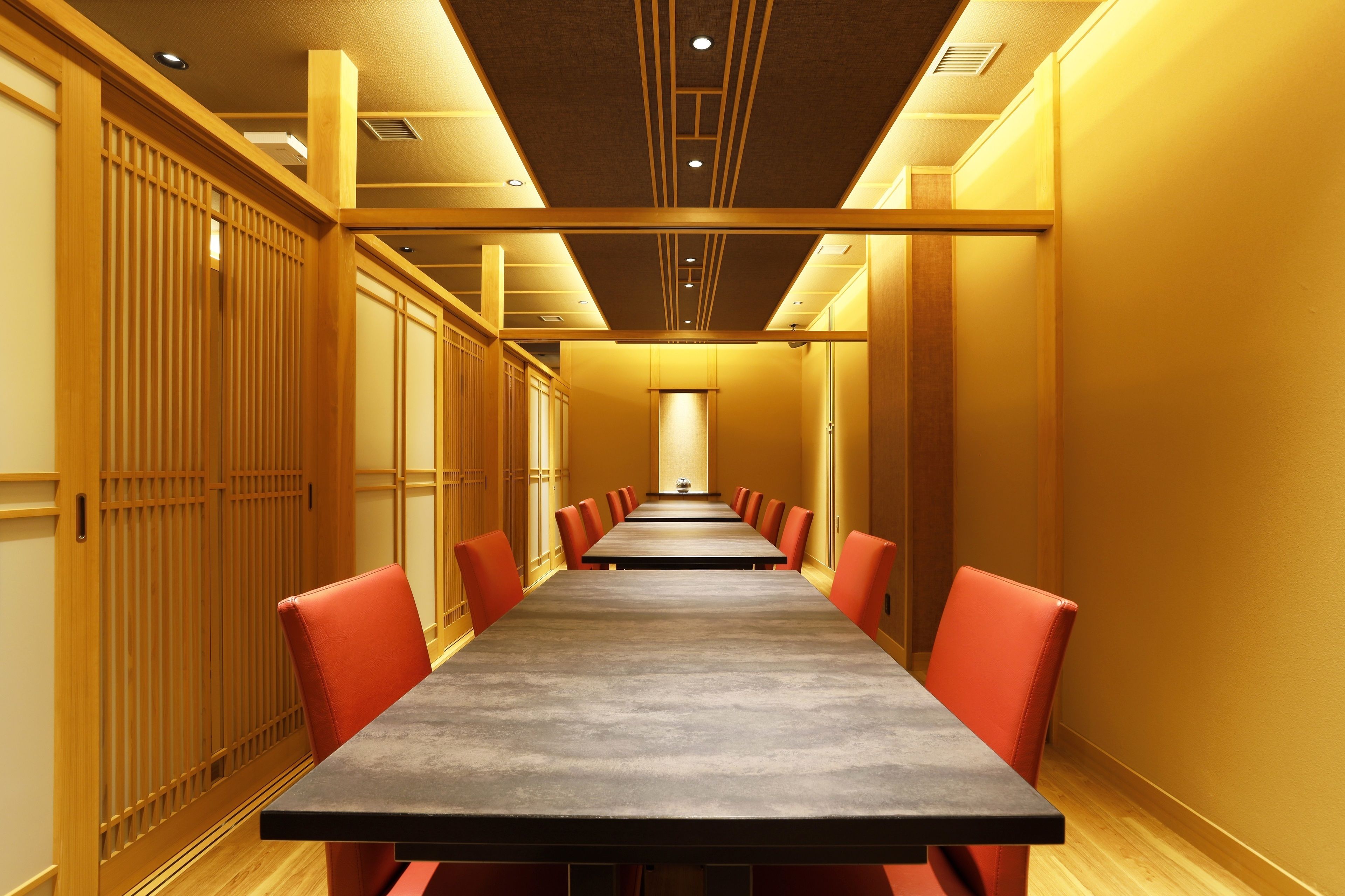 A long conference table with red chairs in a room with wooden paneling and recessed lighting.