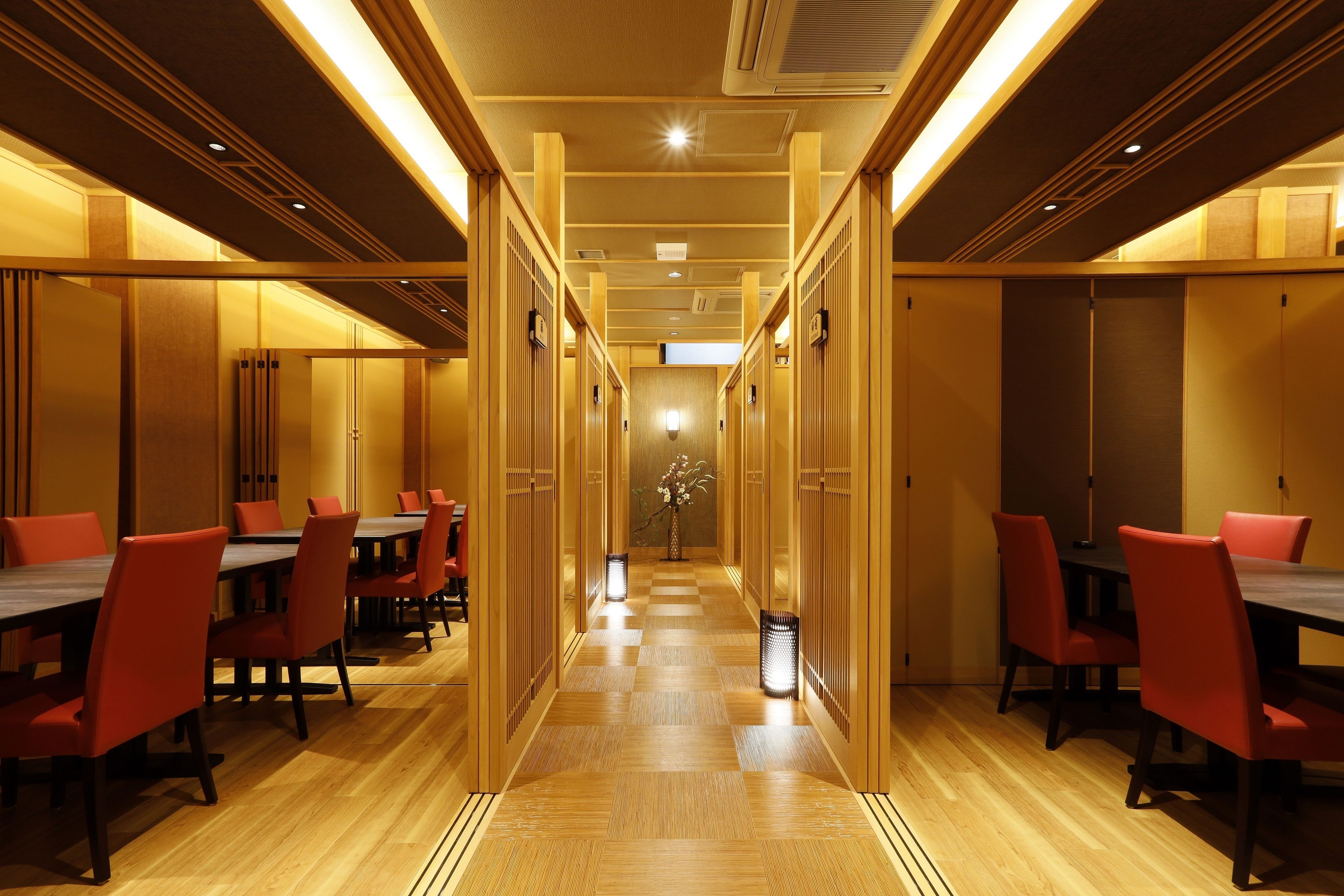 Un pasillo de hotel con paneles de madera, suelo de cuadros y sillas rojas alrededor de mesas.