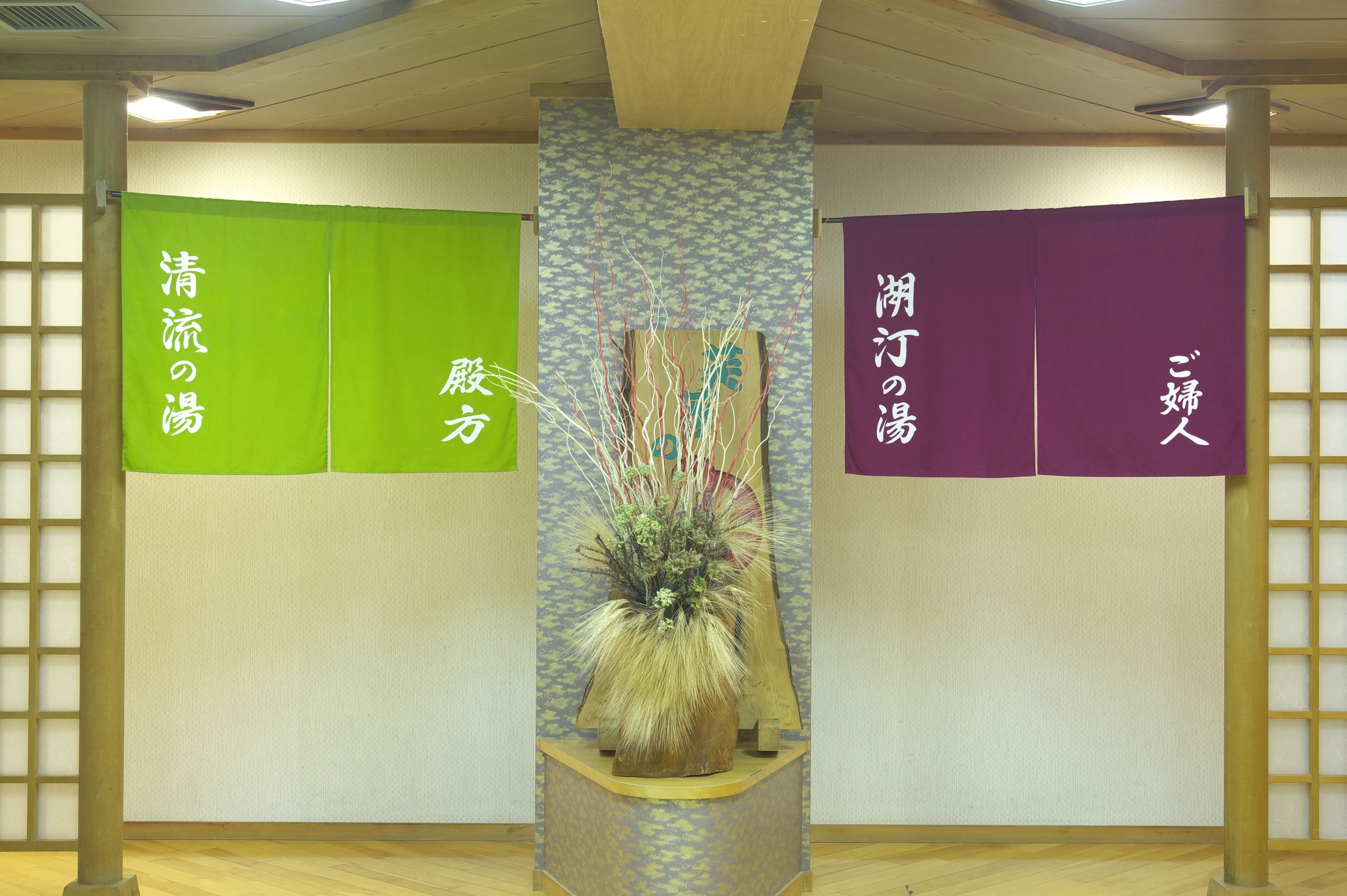 A room with a wooden floor, a central plant, and three vertical panels with Japanese text.