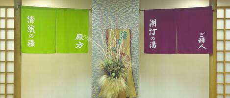 Et værelse med trægulv, en centralt placeret plante og tre lodrette paneler med japansk tekst.