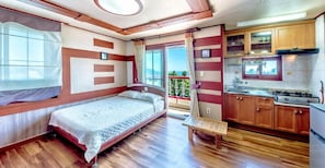 A compact room with a bed, a small bench, a kitchenette, and a balcony with a view.