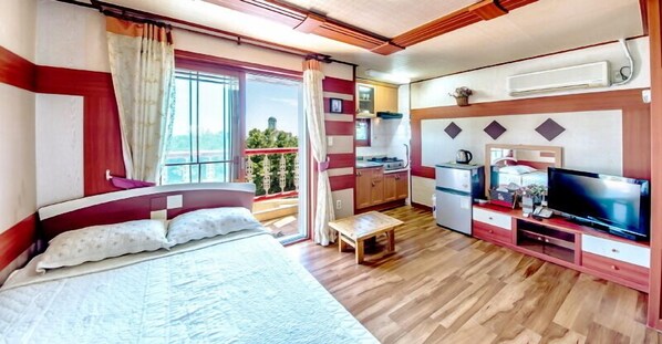 A bedroom with a large bed, a TV, a small table, and a balcony with a view.