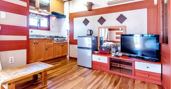 Una cocina compacta con armarios de madera, estufa a gas, refrigerador y televisor sobre un mueble de madera.
