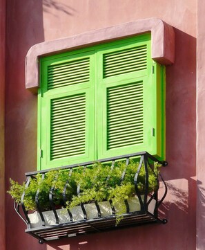 Una ventana con contraventanas verdes y una maceta con follaje verde.