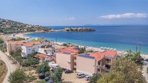 A coastal residential area with buildings featuring red-tiled roofs, solar panels, and a beach with umbrellas. - Castro Deluxe (Sithonia)