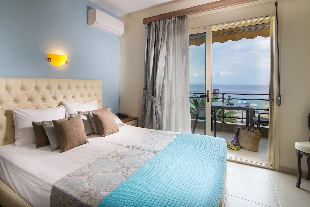 A bedroom with a large bed, a nightstand, a wall-mounted light, and a view of the balcony.