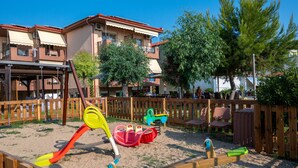 A playground with swings and a slide, surrounded by a wooden fence and trees. - Castro Deluxe (Sithonia)