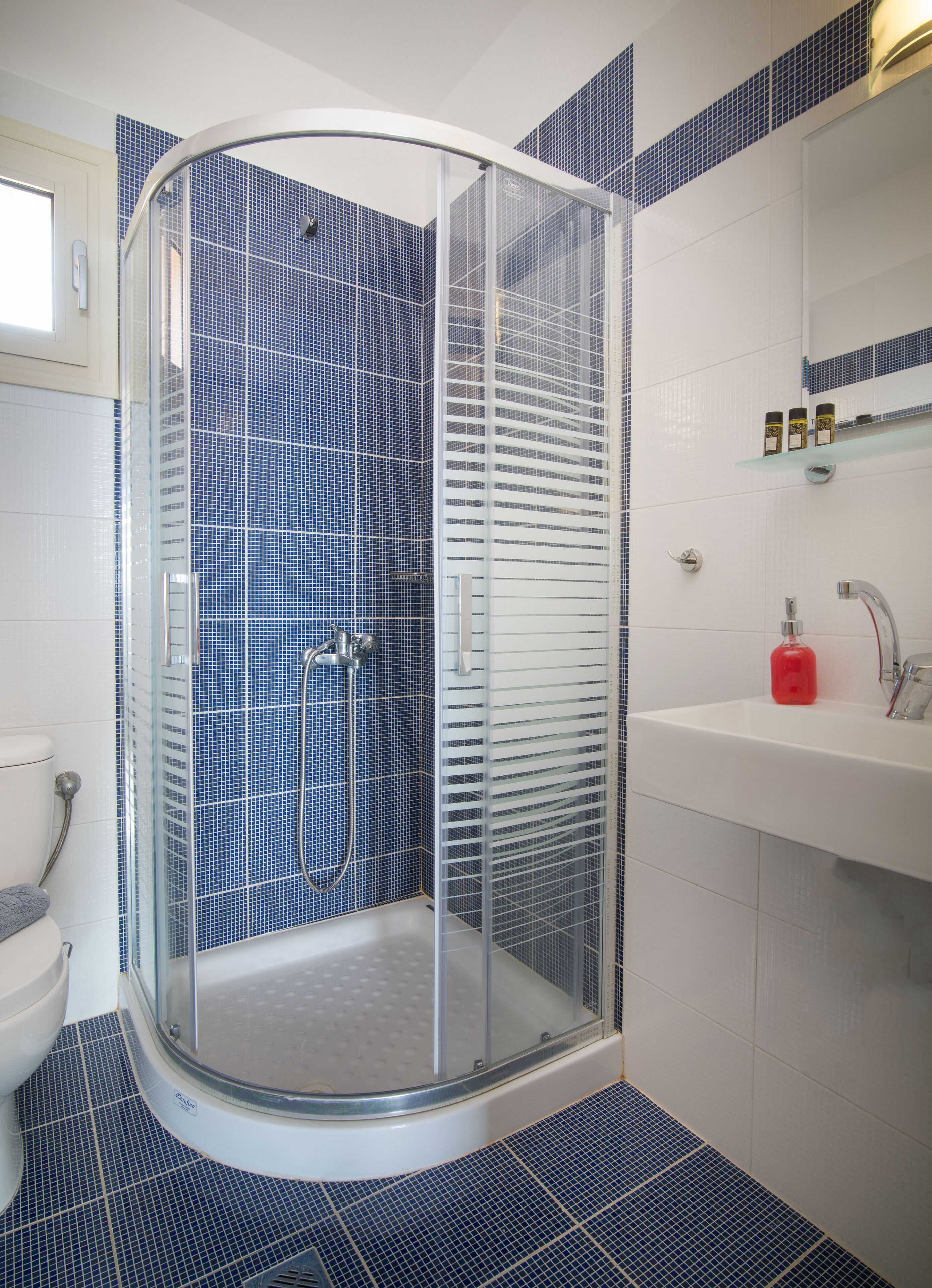 A bathroom with a glass-enclosed shower, a white sink, and blue-tiled walls.