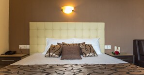 Ein Hotelzimmer mit einem großen Bett, einem Nachttisch mit Telefon, einer Ablage mit Kerzen und einer Wandleuchte.