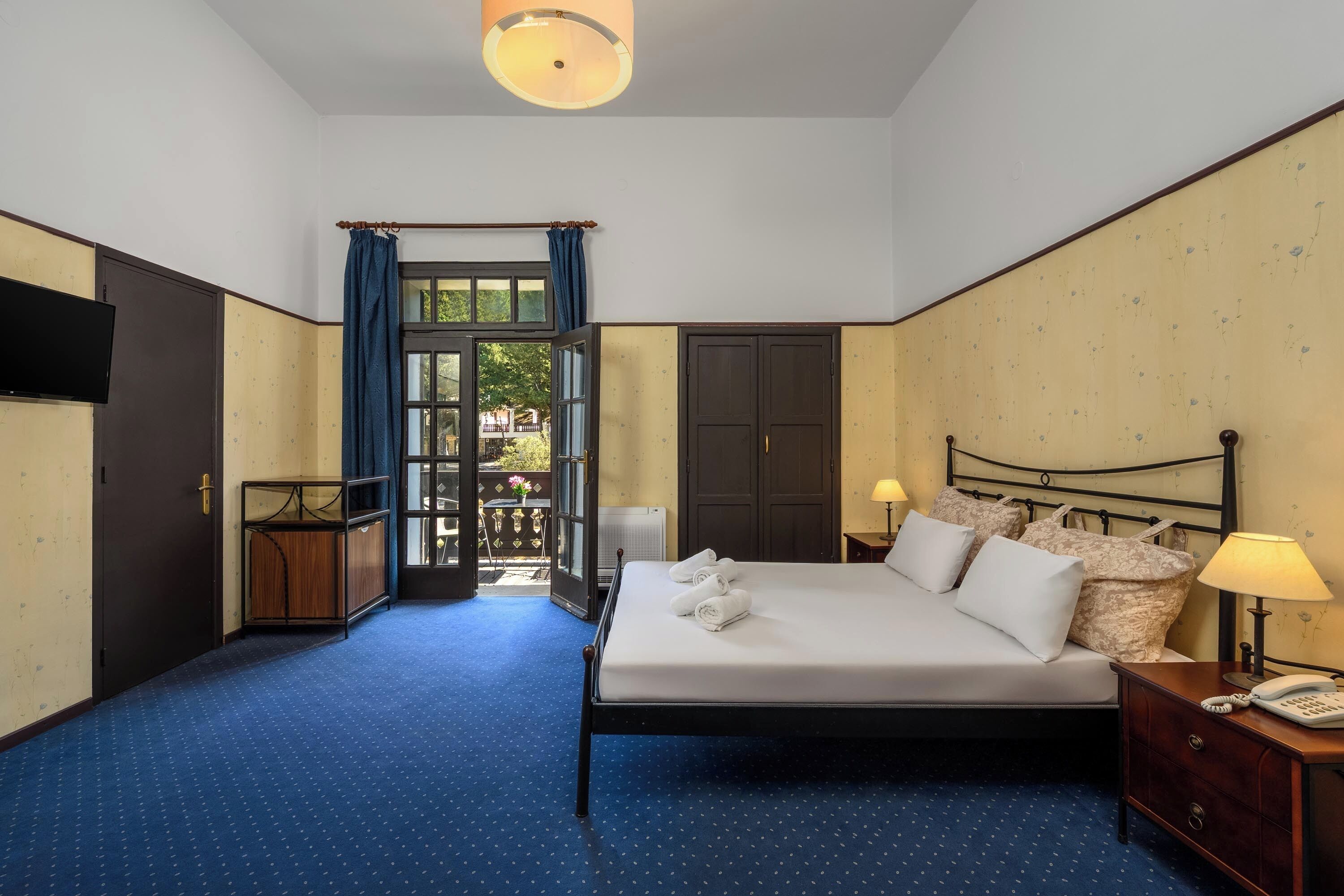 Una camera d'albergo con un letto grande, un comodino con una lampada, un armadio e una televisione appesa al muro.