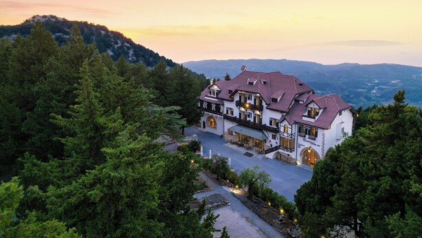 A large, white building with a red roof, surrounded by dense forest, and featuring a spacious courtyard with outdoor seating. - Elafos Hotel (Rhodes)