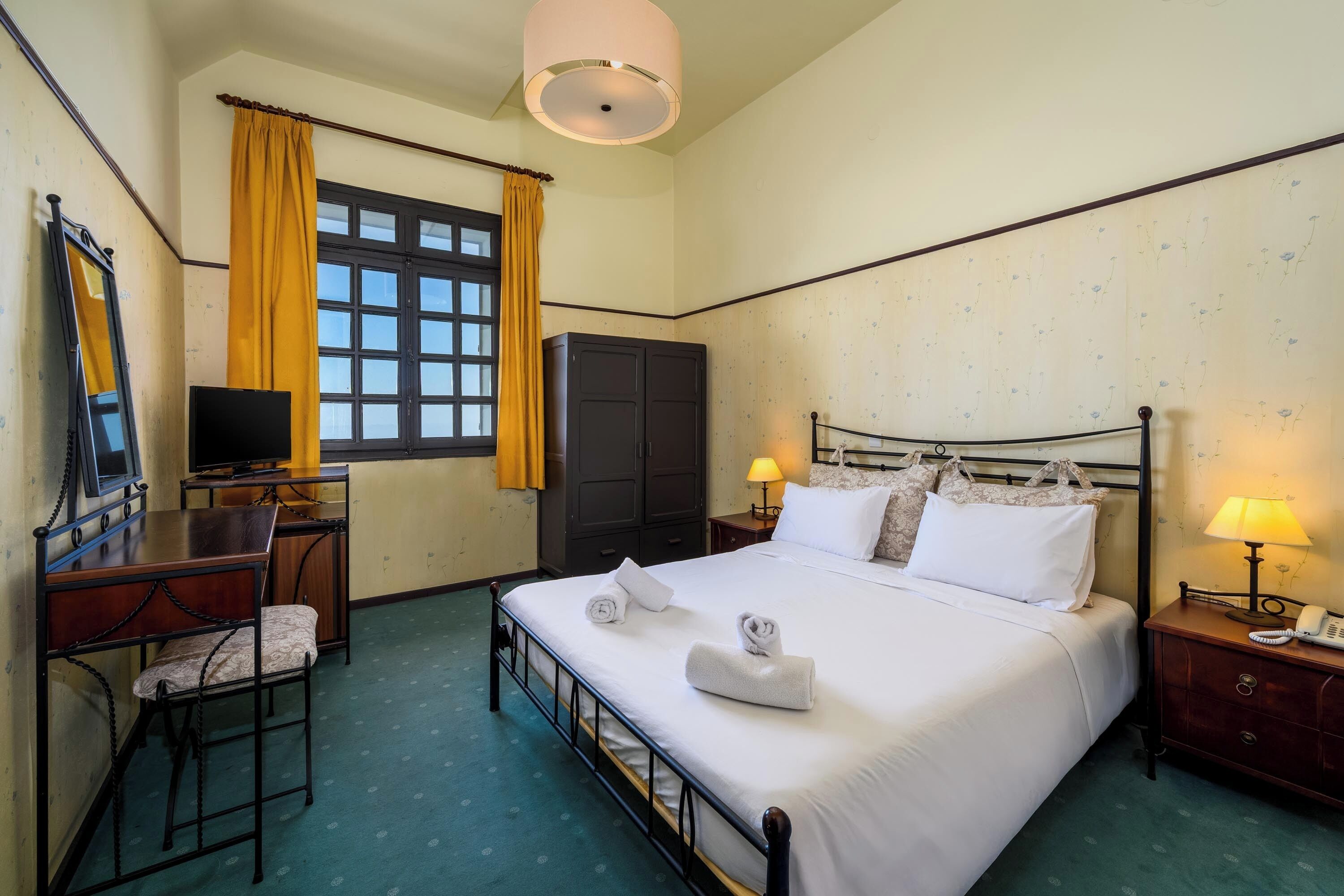 A hotel room with a bed, a desk with a chair, a wardrobe, a television, and a window with curtains.