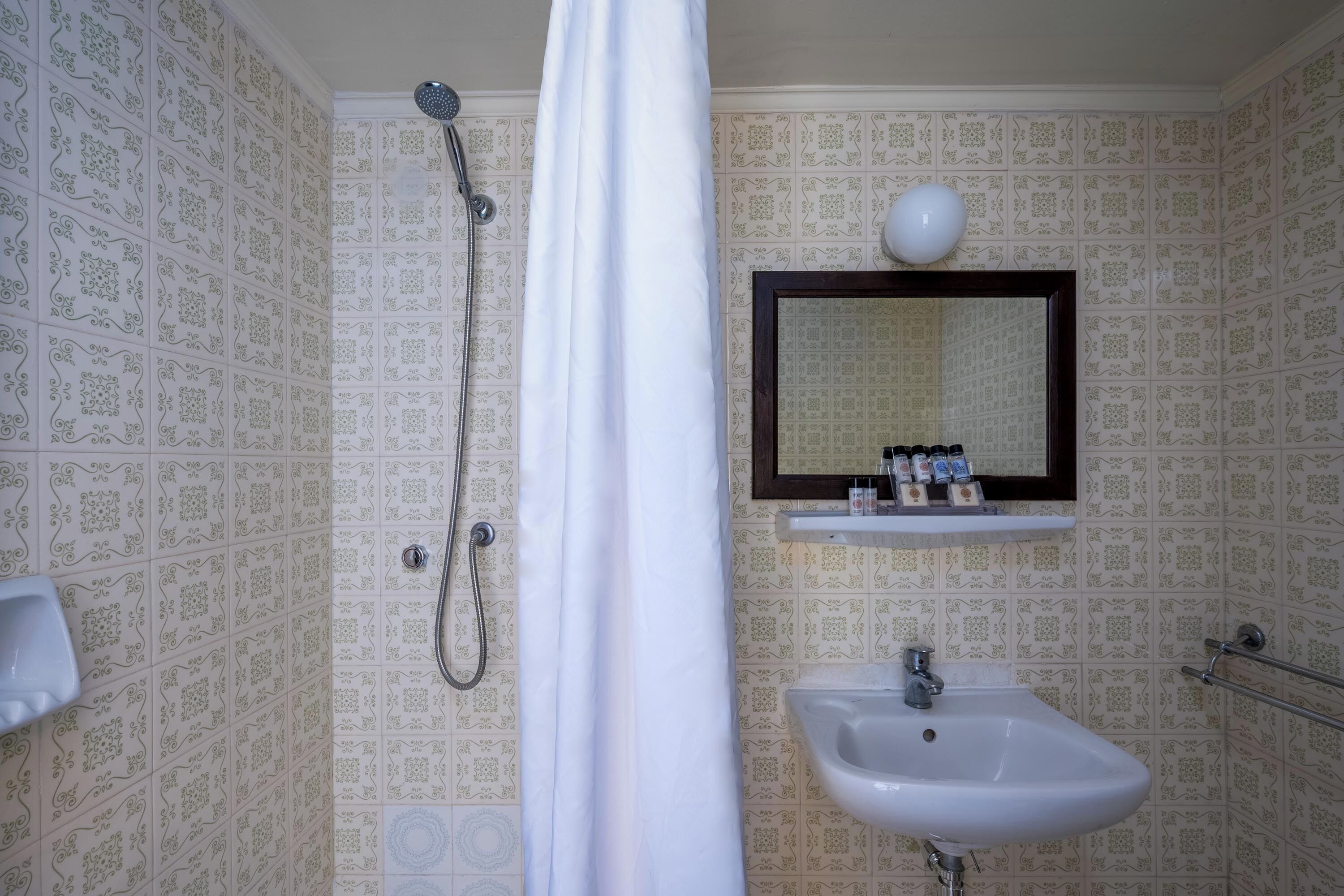 Ein Badezimmer mit strukturiertem Wandpapier, einer Dusche, einem Waschbecken und einem Spiegel mit Ablagefläche darüber.