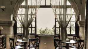 A room with two round tables and chairs, large windows with curtains, and a view of trees outside. - Elafos Hotel (Rhodes)