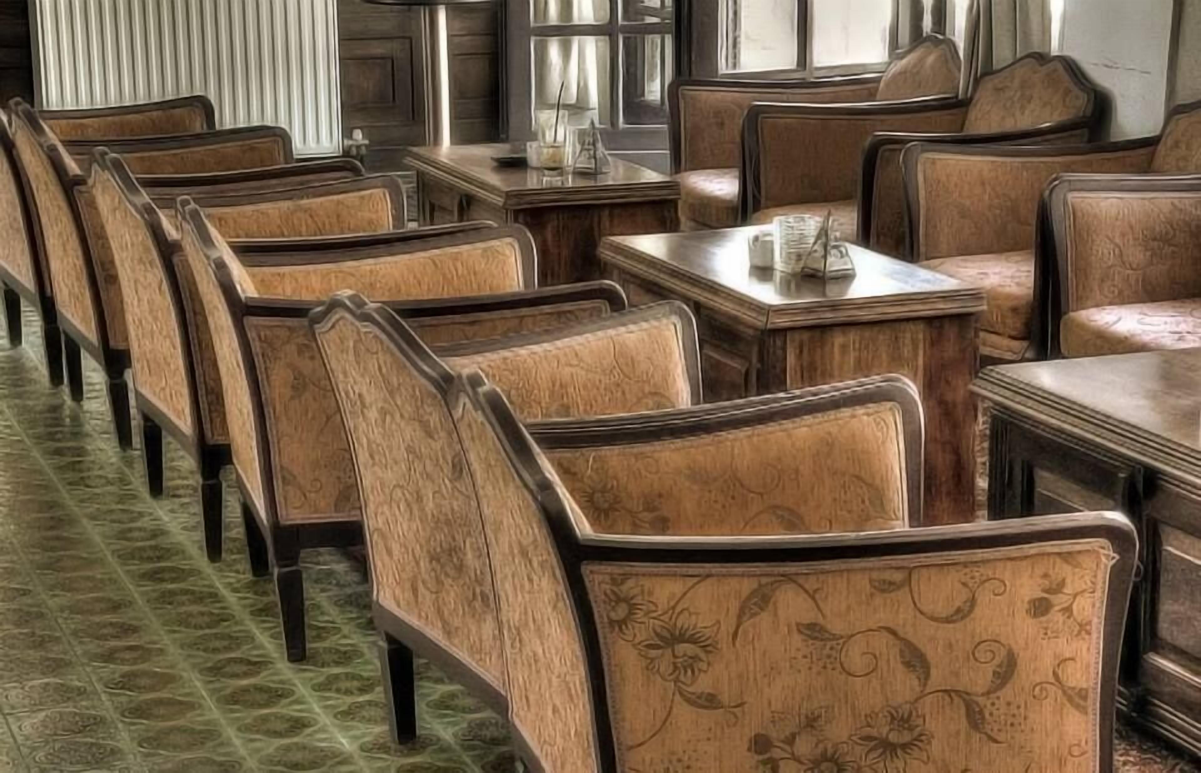 Une rangée de chaises en bois, dotées d’un revêtement floral et posées sur un tapis à motifs verts.