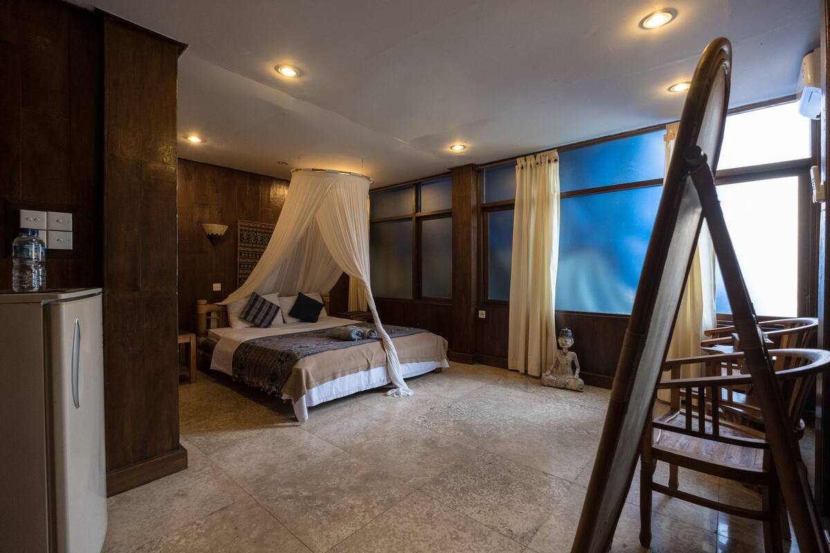 A bedroom with a four-poster bed, a wooden desk, and a large window with curtains.